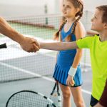 You played well. Close up of tennis trainer shaking hand of glad boy. Children are looking at man with trust and smiling